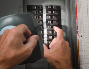 A pair of hands throwing circuit breaker at residential service panel while other hand holds flashlight.