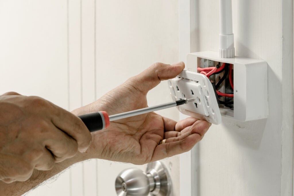 Electrician's hand using screwdriver to replace an outlet on a white wall.